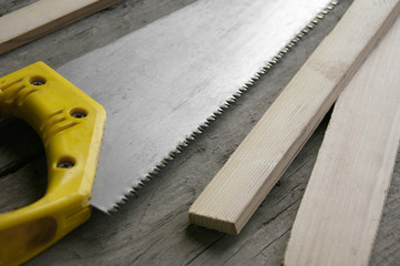 Hacksaw hand on wood with a yellow handle close-up.