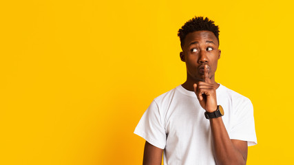 Amazed young african guy keeping finger on lips