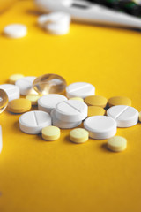 Assorted pharmaceutical medicine pills, tablets and capsules on yellow background.