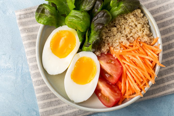 Healthy green vegetarian buddha bowl lunch with eggs, quinoa, carrots,tomato, lettuce leaves, on a blue background., top view.