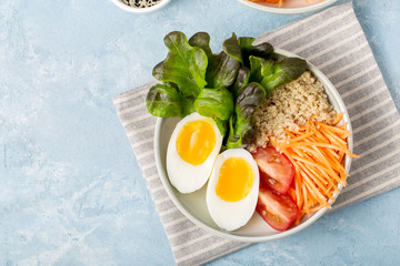 Healthy green vegetarian buddha bowl lunch with eggs, quinoa, carrots,tomato, lettuce leaves, on a blue background, top view