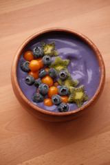 Smoothies of violet color from banana and currant, on top of a blackberry, physalis and kiwi berry. Smoothies in a wooden bowl.