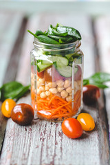 Fresh spring salad of carrots, chickpeas,tomato, cucumbers and spinach in a glass jar for a snack with you. The concept of healthy proper nutrition for the whole family. selective Focus