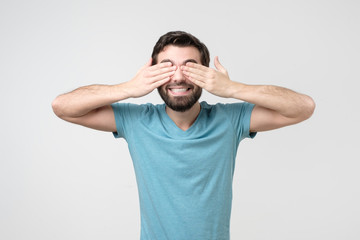Fototapeta premium Young happy hispanic man covering eyes with hands waiting for gift or surprise
