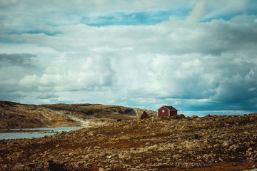 A red wooden house stands against a cloudy stormy sky among the endless expanses of Norway. Atmospheric dramatic Norwegian landscape. Amazing beautiful scandinavian nature. Travel to Norway