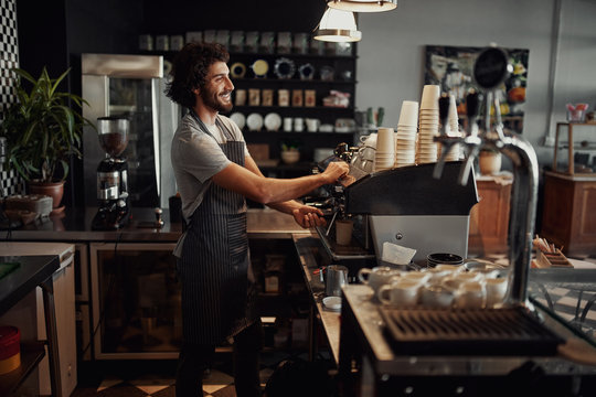 Cheerful caucasian coffee shop owner wearing apron preparing coffee using machine
