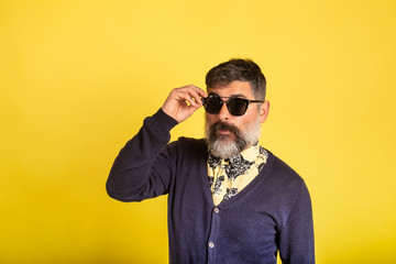 Portrait of man with beard and sunglasses looking towards camera on yellow background