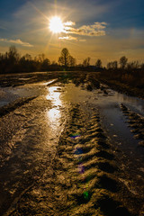 Flooded dirty rural road in a mysterious backlight from the sun giving lens flare