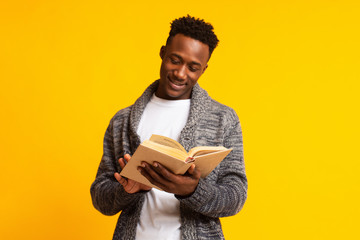 Handsome african guy reading interesting book over yellow