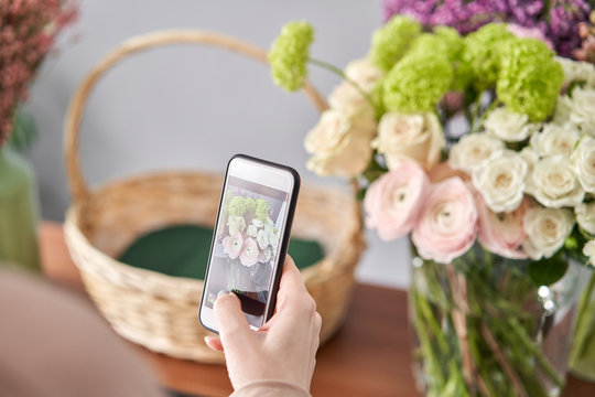 A woman takes a photo on her phone of flowers. Floral shop concept . Florist woman creates flower arrangement in a wicker basket. . Flowers delivery.