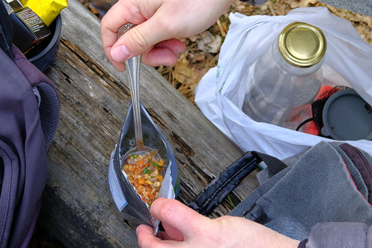 Tourist is eating freeze dried food during resting. Enjoy a tasty food during on a hike. Food in bag for outdoor activities, closeup.