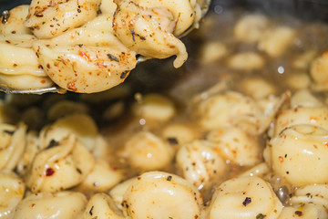 Boiled dumplings with spices on a spoon over a pot of cooked dumplings. Close up.
