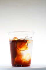 Iced coffee takeaway cup with liquid pouring down into container isolated on white background