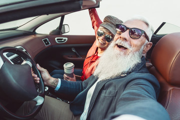 Happy senior couple taking selfie on new convertible car - Mature people having fun together during...