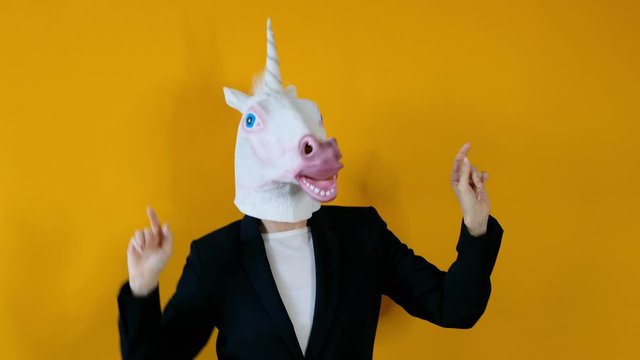Weird funny video - woman in a suit with unicorn head dancing over yellow background