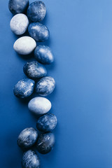 Beautiful group ombre blue Easter eggs with quail eggs and feathers on a blue background. Easter concept. Border eggs. Copy space for text