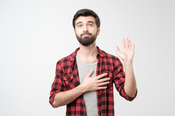 Naklejka premium Sincere hispanic male with beard raising palm and holding hand on chest