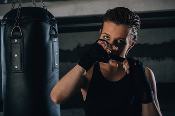 Fototapeta na wymiar Picture of focused young woman preparing her black bandages for boxing inside a garage.