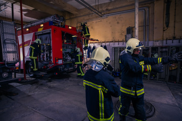 Firefighters preparing their uniform and the firetruck in the background inside the fire station