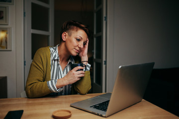 overworked woman sitting home at desk using laptop