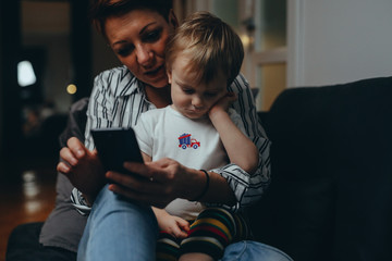 mother and child using mobile phone relaxed on sofa at home