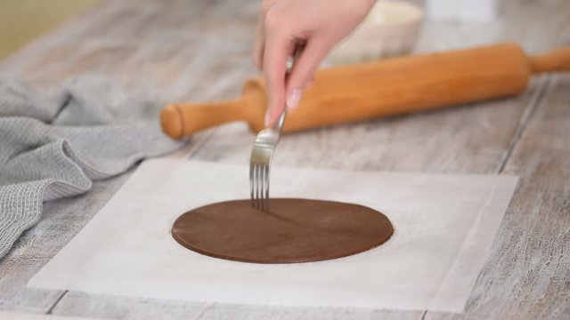 Woman pierces dough with a fork over to prevent air bubbles while baking.