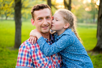 Obraz premium Daughter kissing young happy father in summer park on natural green background. Happy loving family concept
