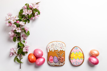 Easter festive arrangement in row of gingerbreads, colored eggs and pink Apple tree twig on white backdrop. Copy space.