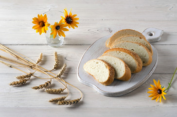 Sliced bread and yellow flowers on white wooden table