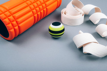 Set of green myofascial release and massage ball, bumpy foam massage roller for trigger points and white belt over grey background. Self body care massage and stress, pain relief. Sport concept. 