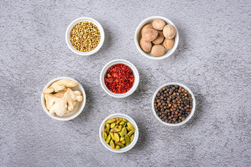 mix of aromatic spices coriander, black pepper, bergamot, dried ginger, nutmeg, paprika in white cups on gray concrete background Top view Flat lay Healthy food