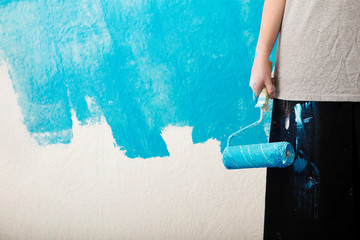 Unfinished wall. Girl holds paint roller in her hand