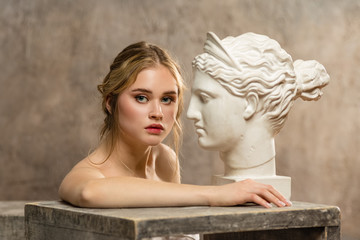 Young woman posing near ancient Greek statue
