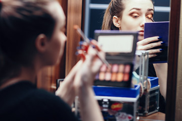 reflection of a beautiful girl in the mirror doing makeup at the dressing table in the room at home, young woman preparing face, concept female beauty and cosmetics