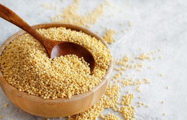 Raw dry hulled millet in a wooden bowl with a spoon - obrazy, fototapety, plakaty
