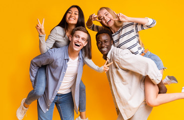 Two international teen couples having fun over yellow background