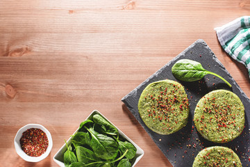 Raw green chicken and spinach burgers with spices on a stone plate in hard light, top view. Eating healthy concept, dinner idea for dieting, weight-loss-friendly foods, rustic style