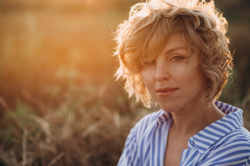 Close-up portrait of a beautiful woman with curly hair in a wheat field in summer at sunset. Soft selective focus. .