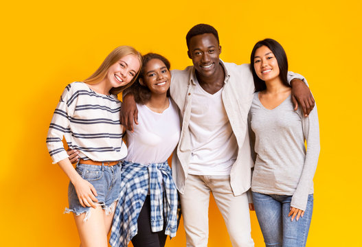 Positive multiethnic teenagers posing over yellow background