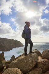 Obraz premium Young woman tourist at Cape Cabo da Roca standing on the rocky edge of the cliff. The waves of the ocean break on the rocks at the bottom of the cliff