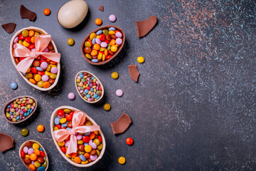 Chocolate Easter border with chocolate eggs and colorful candy sweets on dark concrete black background, copy space. Traditional Easter treats flat lay, holiday background