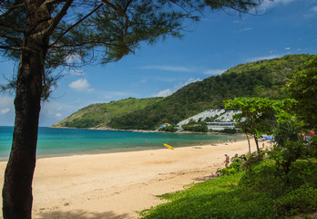 Phuket, Thailand - April 19, 2017. A sandy beach with large stones in the foreground, a green hill and a white hotel.