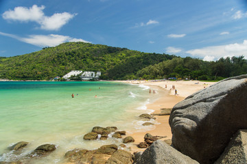 Phuket, Thailand - April 19, 2017. A sandy beach with large stones in the foreground, a green hill and a white hotel.