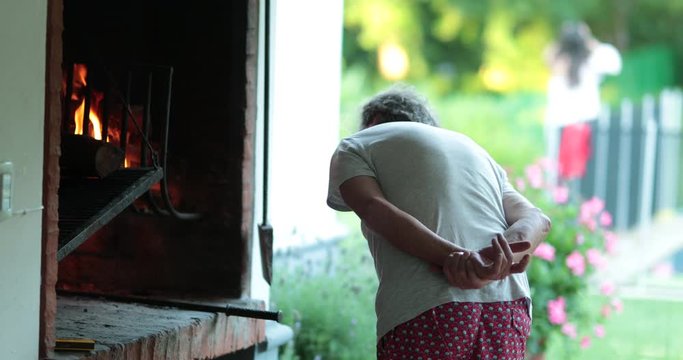 Senior retired man preparing BBQ grill. Older person in front of fire cooking parilla
