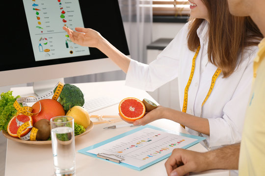 Young nutritionist consulting patient at table in clinic, closeup