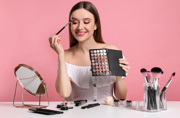 Beauty blogger applying eyeshadow on pink background