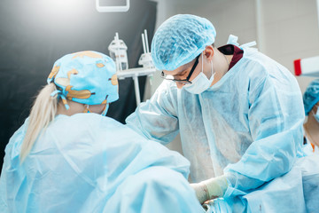 Surgeon performing surgery on breasts in hospital operating room. Surgeon in mask wearing surgical...
