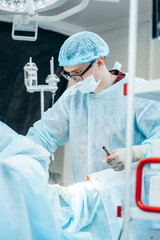 Surgeon performing surgery on breasts in hospital operating room. Surgeon in mask wearing surgical loupes during medical procedure.
