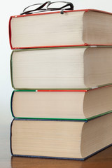 stack of piled books and eyeglasses  rest on a wooden table with copy space for your text