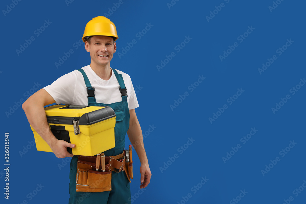 Wall mural handsome carpenter with tool box on blue background. space for text